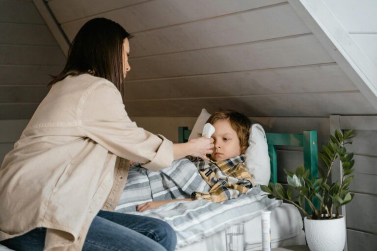 A mother checks her son's temperature, who lies sick in bed, inside a cozy bedroom.